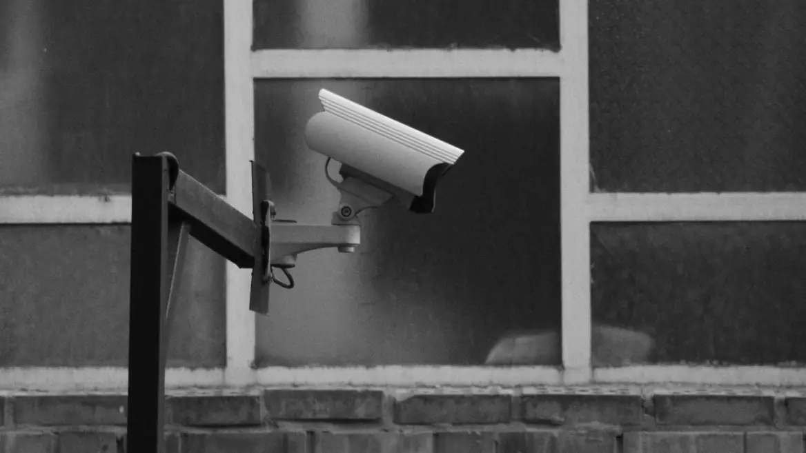 A bullet-style surveillance camera on a wall bracket, in monochrome, facing away from the viewer.