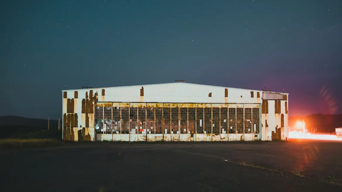 A large commercial building at night, lit from one side, with an empty yard in front of it.
