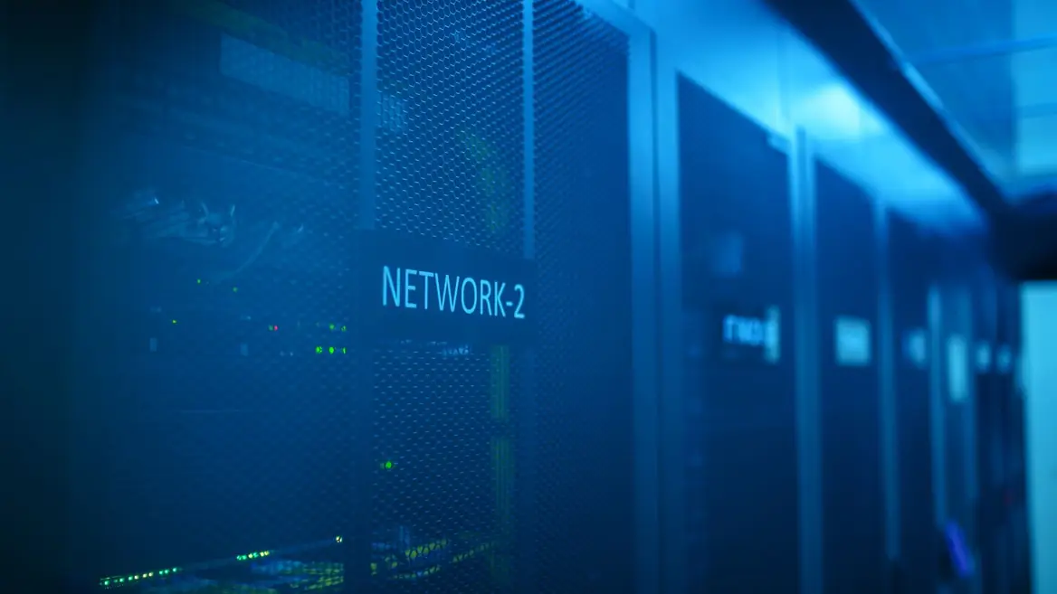 Rows of networking cabinets in a server room, lit blue, status lights showing through mesh doors.