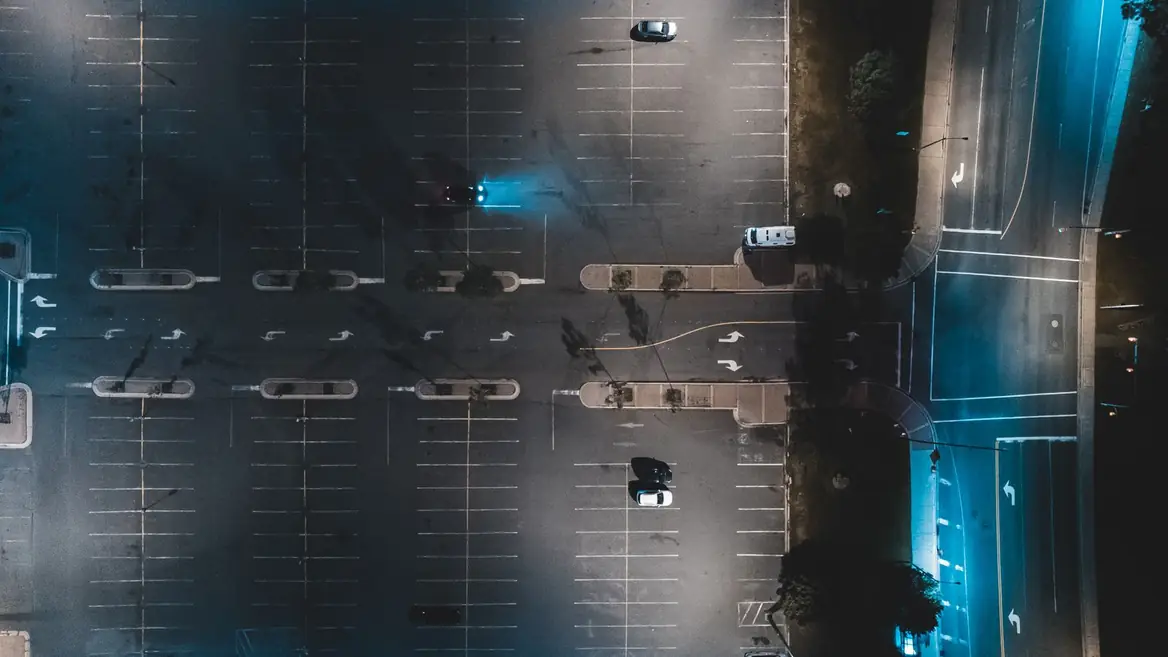 An overhead view of a nearly empty car park at night, lit blue along two edges.